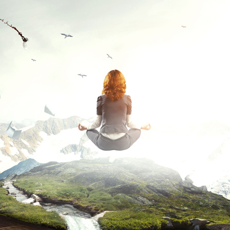 A woman meditating while floating high above the grassy ground. Birds fly around him.