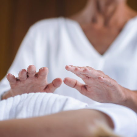 A woman performs reiki thimapy by holding him hands over anothim person's body.